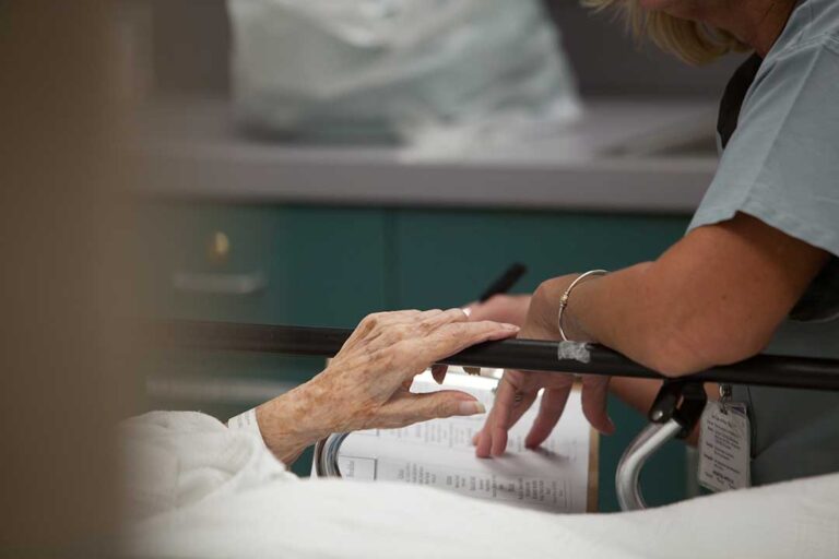 A caregiver assisting an older adult with medication in a bright, home-like setting.